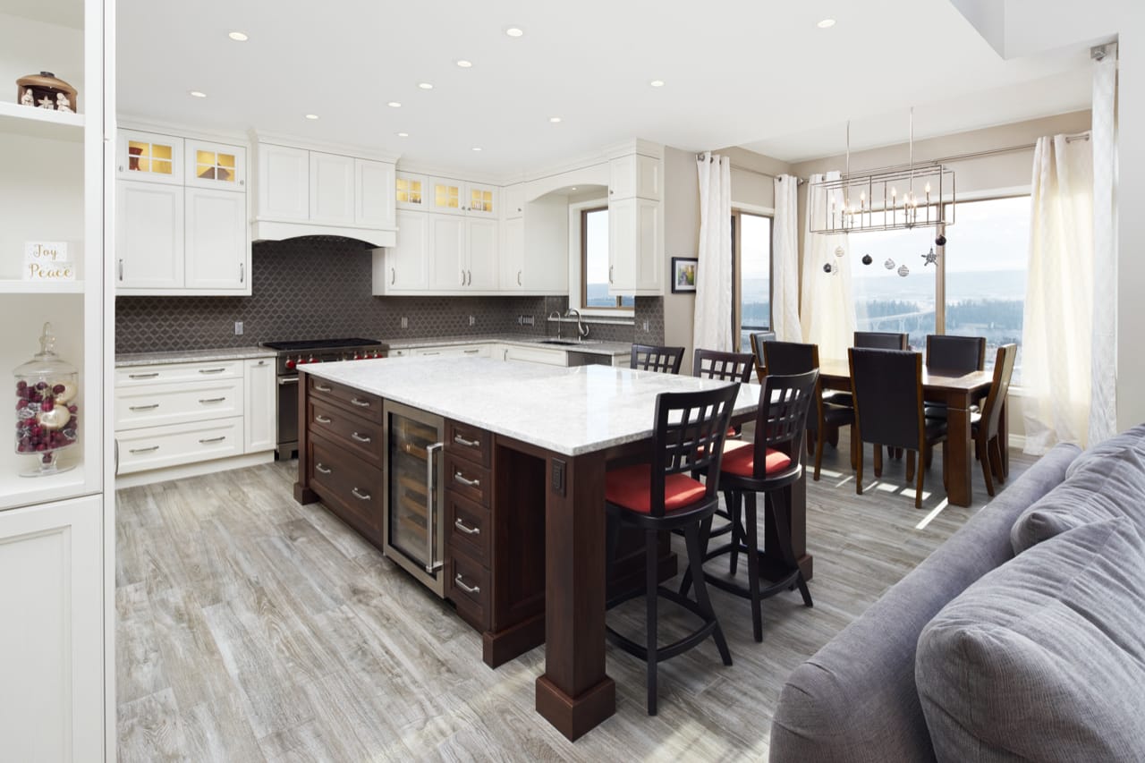 An open-concept kitchen with white perimeter cabinets and a large dark brown island with seating for four.