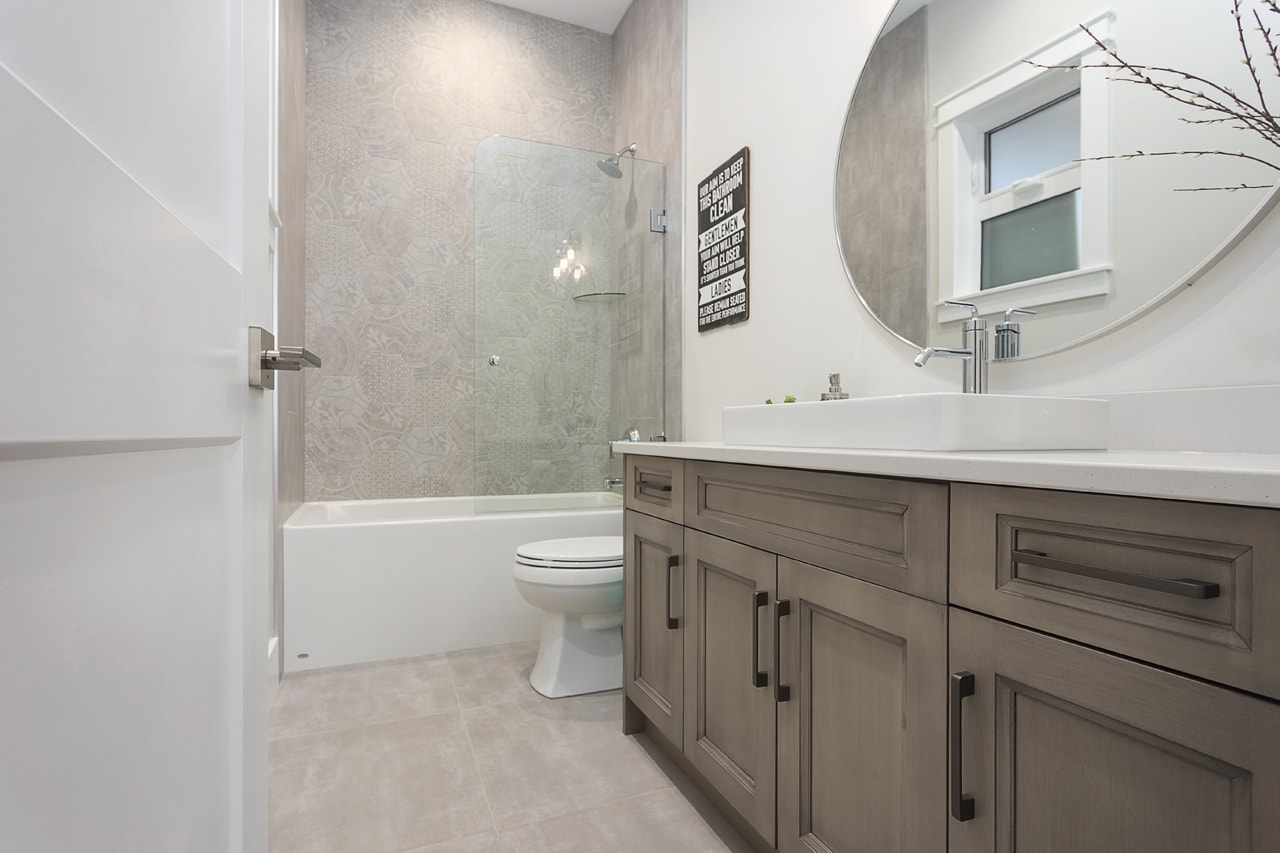 A neutral bathroom with matching soft brown cabinets to the kitchen, with a white quartz countertop and vessel sink.