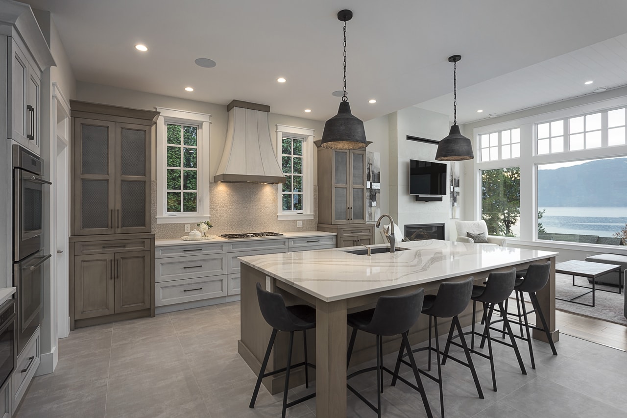A transitional style kitchen with creamy white and beige cabinetry with a custom hood fan.