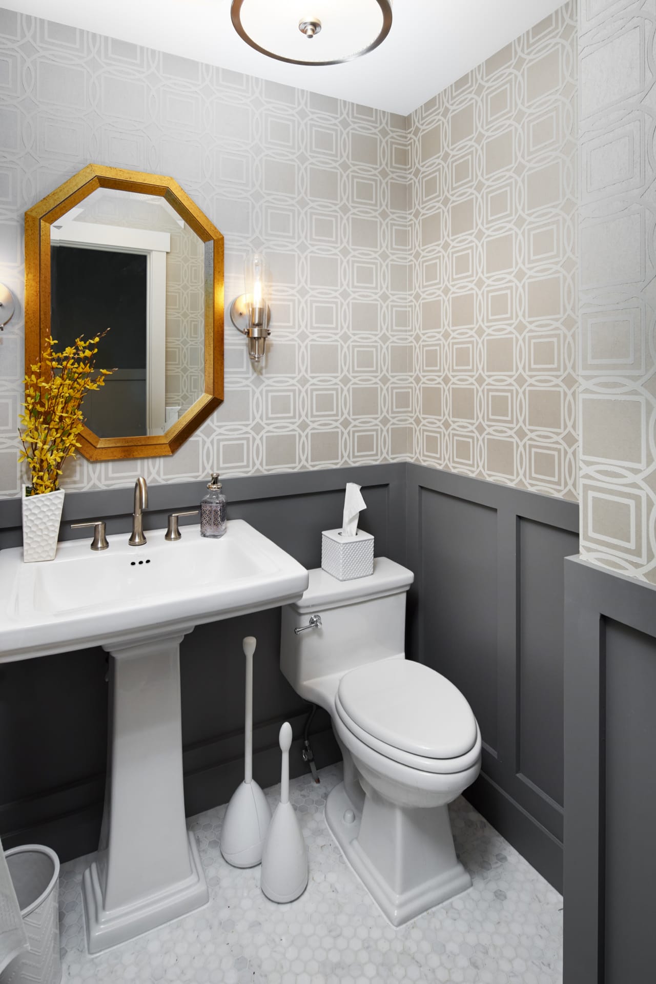 A half bathroom with grey wall paneling, geometric wallpaper and a gold mirror.