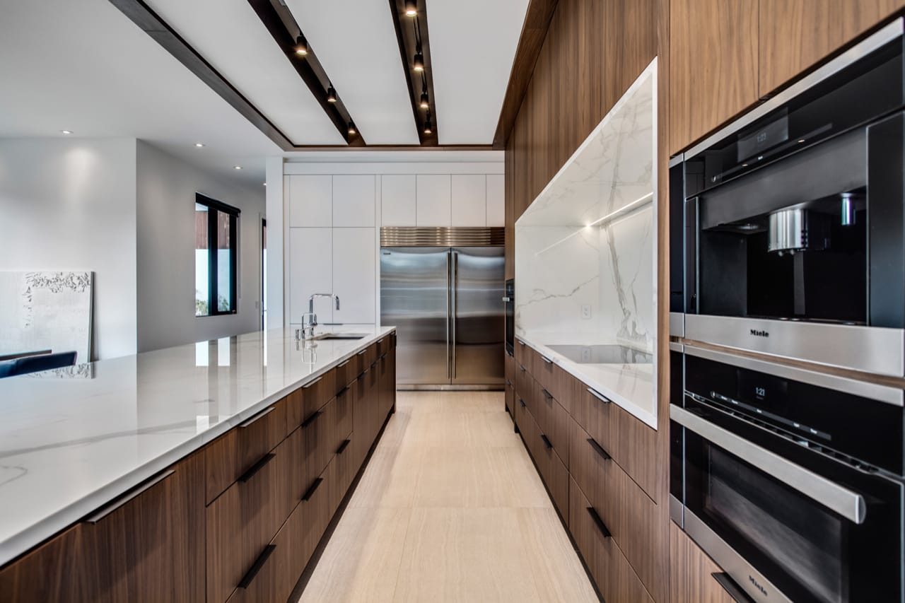 Contemporary white and walnut kitchen with slab cabinetry facing the fridge.
