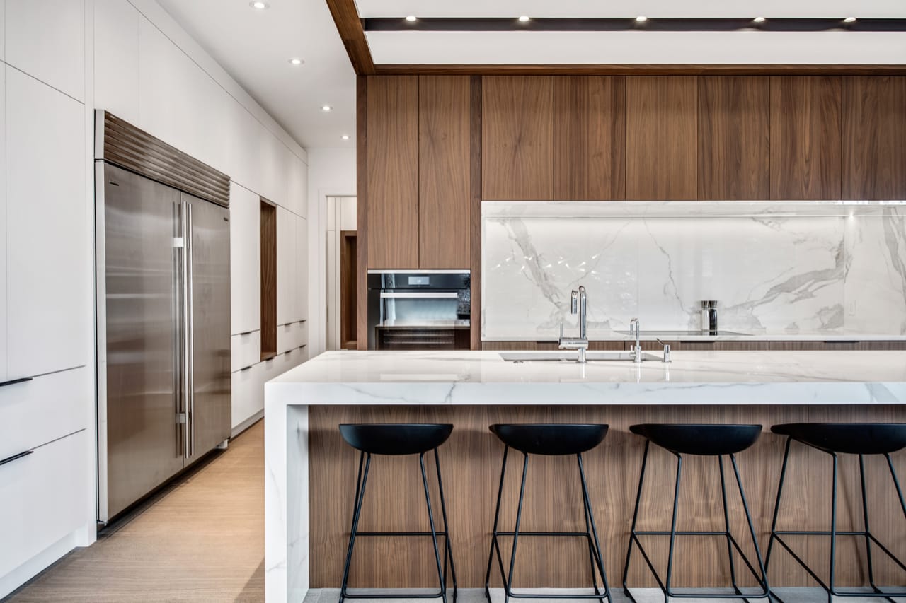 Contemporary kitchen with white and walnut cabinetry with an oversized island with a white porcelain waterfall countertop.