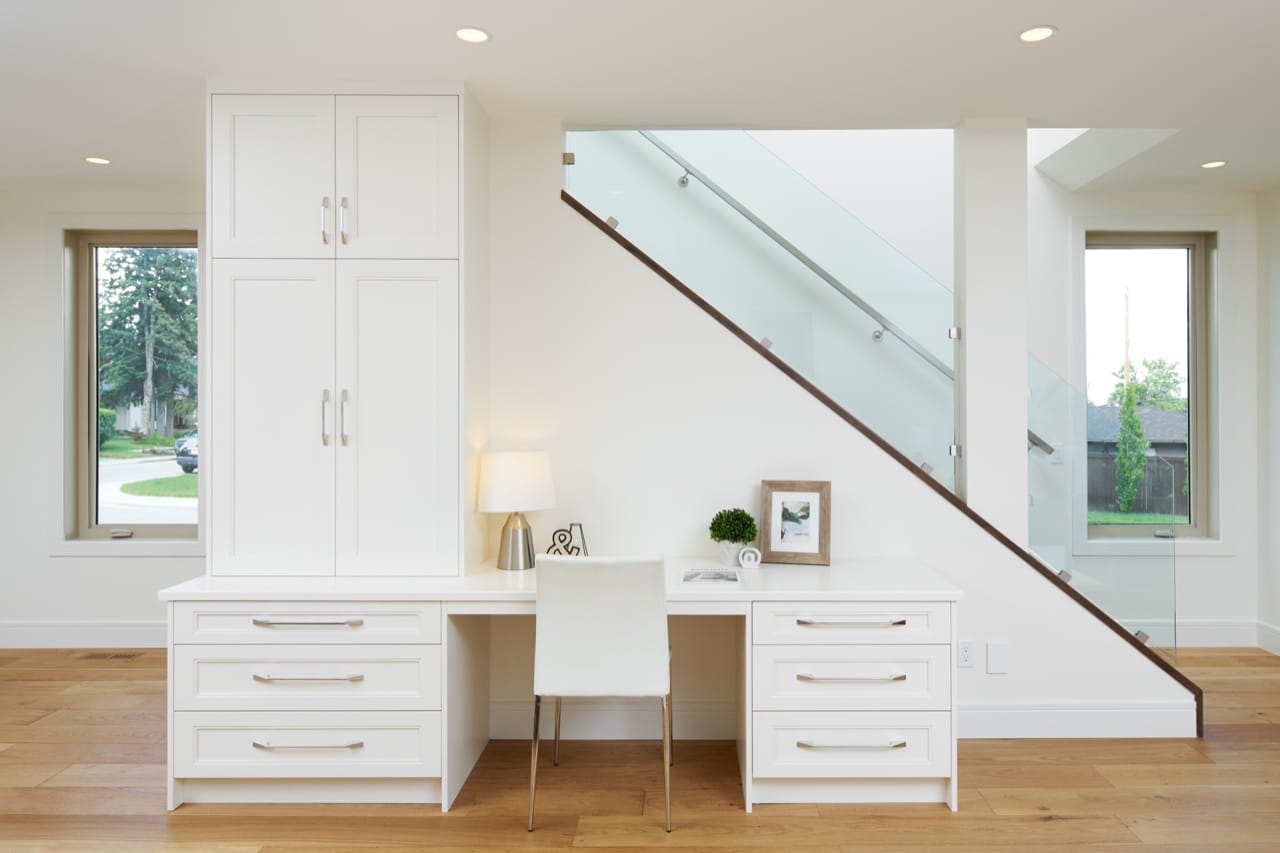 Large white desk with white shaker-style drawers plus a tall bank of cabinetry.