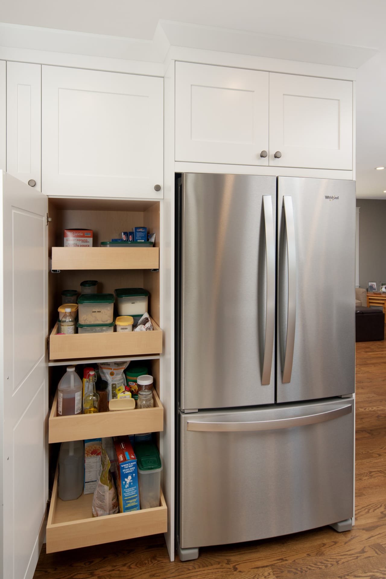 White shaker-style kitchen pantry with pull-out shelves beside a fridge.